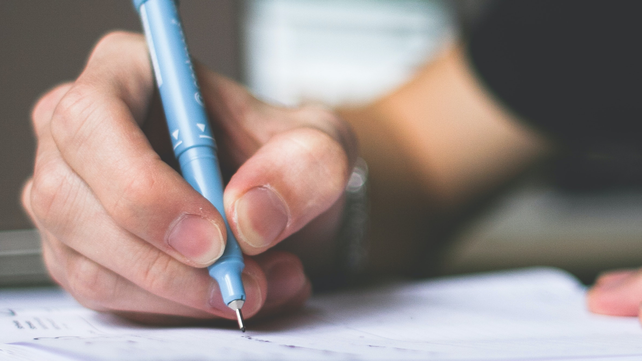 Persona escribiendo en una hoja de papel con un bolígrafo
