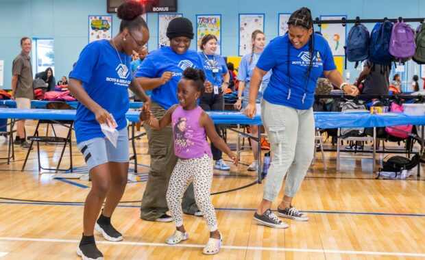 Boys & Girls Club volunteers dance with a young child