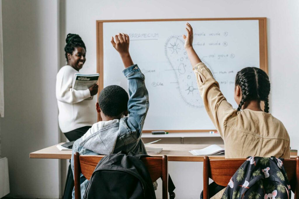 Kids back to school raising their hands in their teacher's classroom