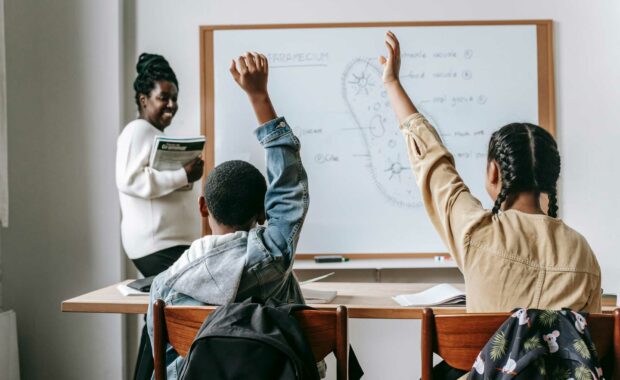 Kids back to school raising their hands in their teacher's classroom